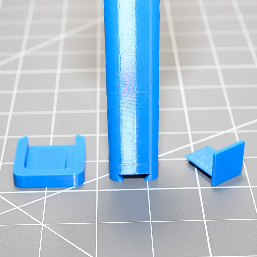 The base of the blue handle with two baseplate options beside it. One is a flat square that allows the unit to sit nicely on a flat surface. The other is a small "L" shaped bracket that lets you glue an avatar to it and connect it at the bottom.
